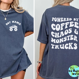 May include: Dark blue t-shirt with white text and graphic. The front of the shirt says "BOY MAMA" with a monster truck graphic. The back says "POWERED BY COFFEE CHAOS & MONSTER TRUCKS".