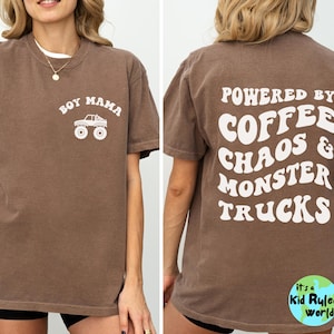 May include: Brown t-shirt with white text and graphics. The front says "BOY MAMA" above a monster truck graphic. The back says "POWERED BY COFFEE CHAOS & MONSTER TRUCKS". A small logo is at the bottom.