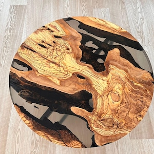 Pode incluir: Tampo de mesa redondo de madeira com enchimento de resina epóxi preta. A madeira tem um padrão de grão natural e é de cor castanho claro. A resina é transparente e tem um acabamento liso.