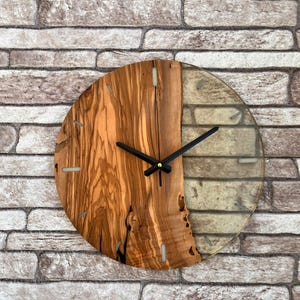 May include: A round wooden and clear resin wall clock with black hands. The clock face is half wood and half clear resin.