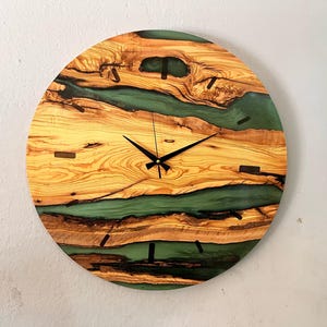 May include: A round wooden clock with a green and brown epoxy resin design. The clock face has black hands and a black outline.