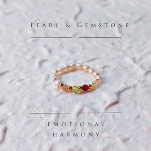 Può includere: Un anello delicato con una fascia di piccole perle color crema. L'anello è impreziosito da perline color oro e una fila di pietre preziose colorate: pesca, verde e rosso. Il testo sull'immagine recita "PEARL & GEMSTONE" e "EMOTIONAL HARMONY".