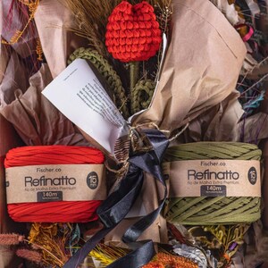 Peut inclure: Un bouquet compos&eacute; d'une tulipe crochet&eacute;e rouge &agrave; tige verte envelopp&eacute;e dans du papier kraft, accompagn&eacute; de deux bobines de fil Fischer.co Refinatto 15mm extra premium rouge et vert olive, chacune de 140m, nou&eacute;es par un ruban noir.