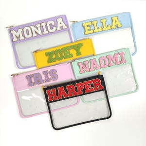 May include: Six clear plastic zippered pouches with colorful fabric inserts. The inserts have names written on them in sparkly letters: Monica, Ella, Zoey, Naomi, Iris, and Harper.
