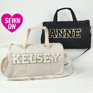 Puede incluir: Dos bolsas de lona beige y negra con letras de purpurina dorada. La bolsa beige tiene el nombre "Kelsey" y la bolsa negra tiene el nombre "Anne".