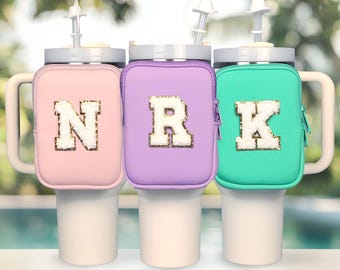 Puede incluir: Tres portavasos aislados con cierre de cremallera. Los portavasos son de color rosa claro, lavanda y turquesa. Cada portavasos tiene una letra blanca grande con purpurina dorada. Las letras son N, R y K.