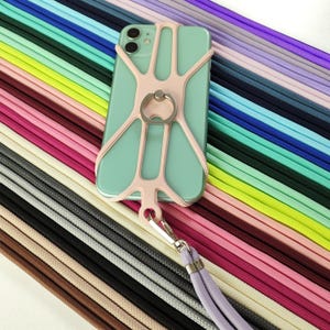 May include: A mint green smartphone with a light pink phone grip and a silver ring holder. The phone is attached to a light purple lanyard with a silver clasp. The background features a variety of colorful cords.