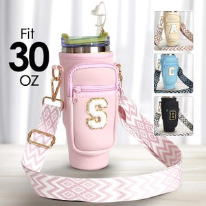 Peut inclure: Tumbler isotherme rose de 30 oz avec une poche zippée et une lettre dorée "S" sur le devant. Le tumbler est doté d'une sangle réglable à motif blanc et rose.