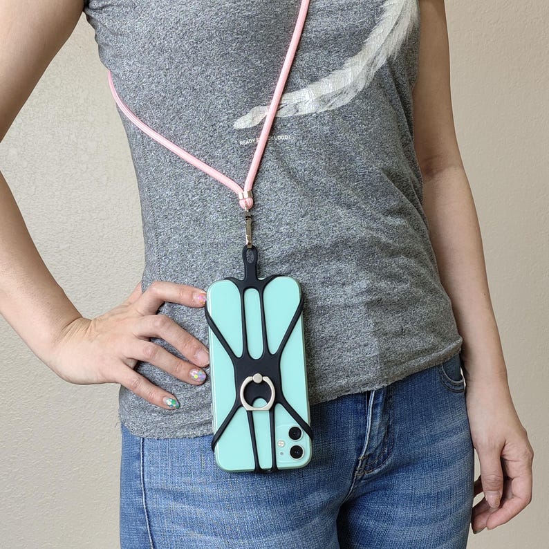 May include: A black phone case with a built-in ring holder and a pink lanyard. The case is attached to a phone with a light blue screen.