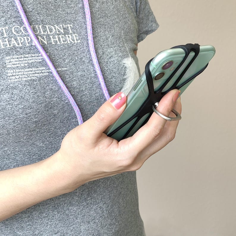 May include: A teal colored smartphone with a black phone grip and a silver ring holder. The phone is attached to a purple lanyard.