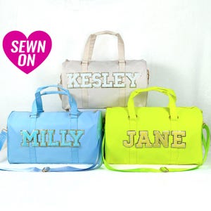 May include: Three canvas duffel bags with personalized names in gold glitter letters. The bags are in light blue, cream, and neon green.