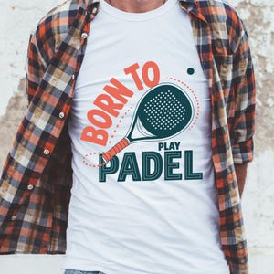 May include: White t-shirt with a padel racket graphic and the text "BORN TO PLAY PADEL" in orange and teal. The shirt has a crew neck and is worn with a plaid button-down shirt.