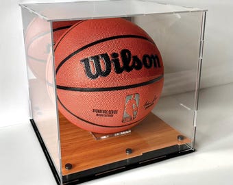 May include: Clear acrylic basketball display case with a wooden base and black trim. The case holds a basketball, showcasing the Wilson logo and NBA branding. The text at the bottom reads: Basketball is for demonstration, and is not included.