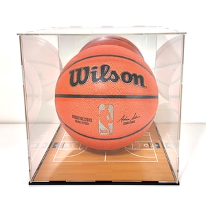 May include: An orange Wilson NBA Signature Series basketball inside a clear acrylic display case. The basketball has the Wilson logo and NBA logo. The case has a basketball court design on the base.