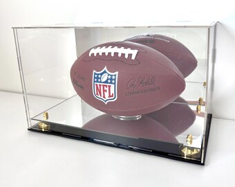 May include: A brown NFL football inside a clear acrylic display case. The football has white laces and the NFL logo. The case has a black base and gold-colored hardware.