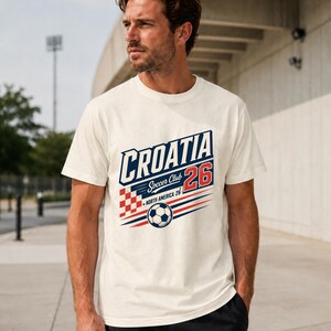 K&ouml;nnte beinhalten: Ein cremefarbenes Kurzarm-T-Shirt mit einem Grafikdruck, der CROATIA Soccer Club 26 NORTH AMERICA 26 liest. Das Design enth&auml;lt ein rot-wei&szlig; kariertes Quadrat, einen Fu&szlig;ball und rote sowie blaue horizontale Geschwindigkeitslinien.