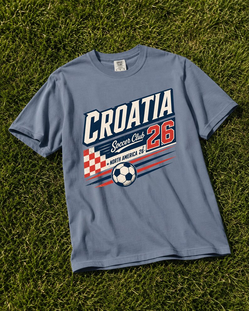 K&ouml;nnte beinhalten: Ein schieferblaues Kurzarm-T-Shirt mit einem Grafikdruck, der CROATIA Soccer Club 26 NORTH AMERICA 26 liest. Das Design umfasst ein rot-wei&szlig; kariertes Quadrat, einen Fu&szlig;ball sowie rote und blaue Bewegungslinien auf der Vorderseite.