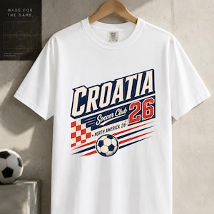 K&ouml;nnte beinhalten: Ein wei&szlig;es kurz&auml;rmeliges T-Shirt mit einem Grafikdruck, der CROATIA Soccer Club 26 NORTH AMERICA 26 zeigt. Das Design umfasst ein rot-wei&szlig; kariertes Quadrat, einen Fu&szlig;ball sowie blaue und rote horizontale Linien auf der Vorderseite.