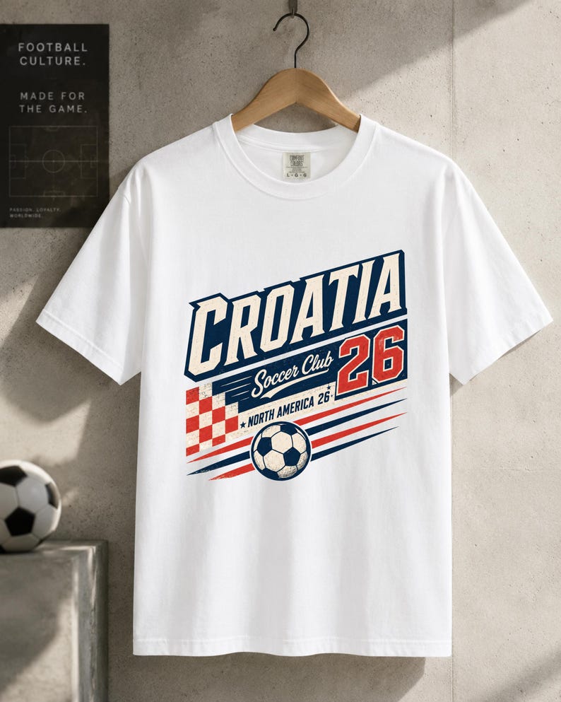 K&ouml;nnte beinhalten: Ein wei&szlig;es kurz&auml;rmeliges T-Shirt mit einem Grafikdruck, der CROATIA Soccer Club 26 NORTH AMERICA 26 zeigt. Das Design umfasst ein rot-wei&szlig; kariertes Quadrat, einen Fu&szlig;ball sowie blaue und rote horizontale Linien auf der Vorderseite.