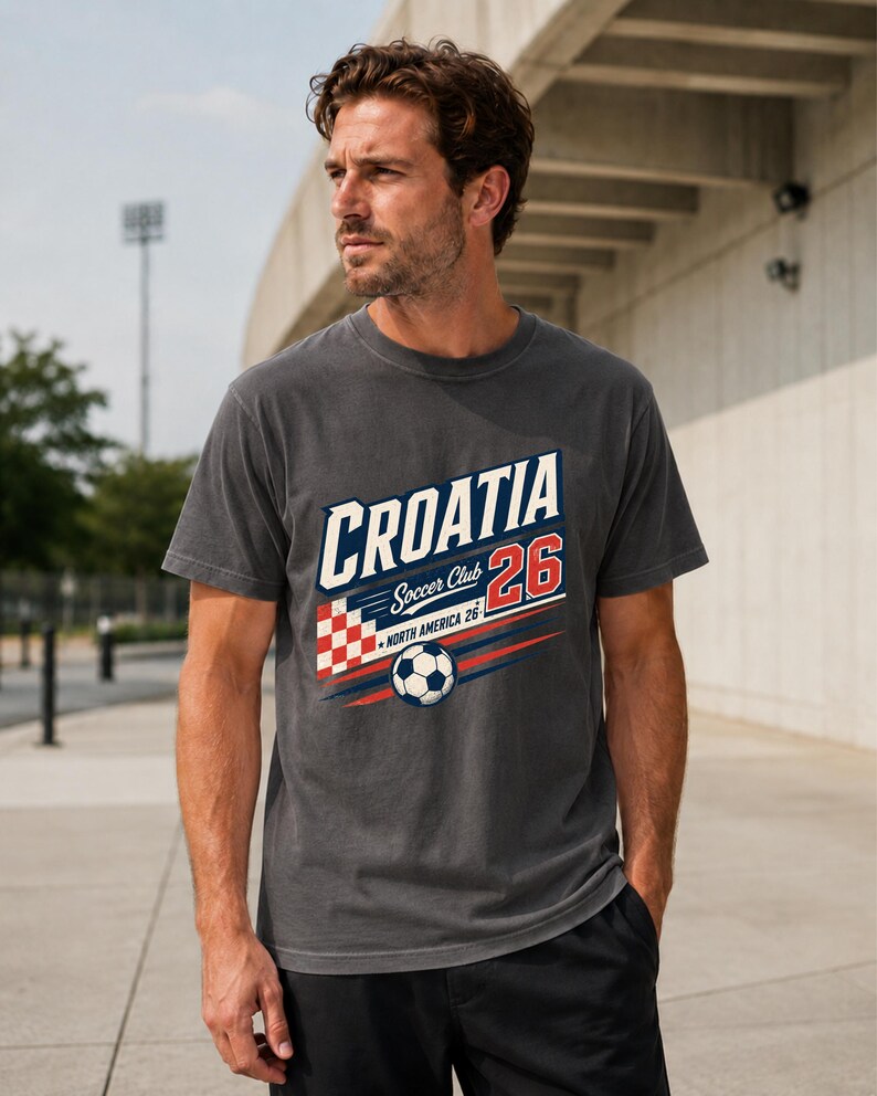K&ouml;nnte beinhalten: Ein anthrazitfarbenes Kurzarm-T-Shirt mit einem Grafikdruck, der CROATIA Soccer Club 26 NORTH AMERICA 26 zeigt. Das Design enth&auml;lt ein rot-wei&szlig;es Karomuster, einen Fu&szlig;ball sowie blaue und rote horizontale Bewegungslinien.