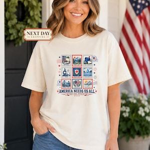 May include: A cream-colored short-sleeve t-shirt featuring a graphic print of nine postage stamp-style illustrations depicting various public services. Below the stamps, the text reads AMERICA NEEDS US ALL and PUBLIC GOOD. PROTECTED.