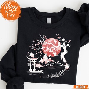 A black sweatshirt with a graphic design depicting a cherry blossom tree with a large red moon in the background.