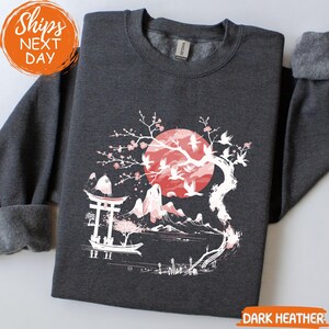 A gray sweatshirt with a graphic design depicting a cherry blossom tree with a red moon and mountains in the background.