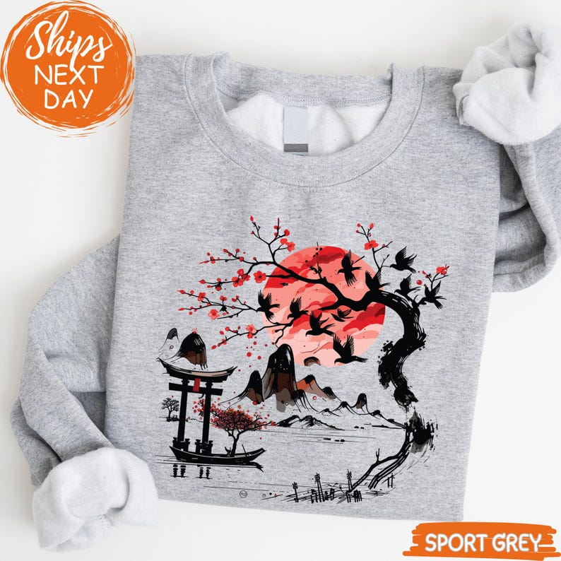 Gray sweatshirt with a graphic design depicting a cherry blossom tree with red flowers, a torii gate, mountains, and a sunset.
