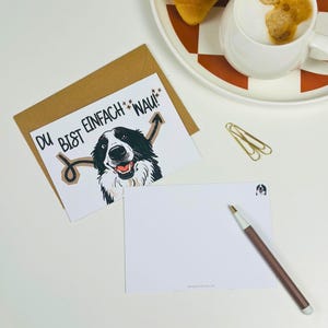 Könnte beinhalten: Eine weiße Grußkarte mit einer schwarz-weißen Hundeillustration, dem Text DU BIST EINFACH WAU! und braunen Pfeilgrafiken, dazu ein brauner Umschlag, ein Kugelschreiber, zwei goldene Büroklammern und eine weiße Keramiktasse.