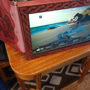 May include: A wooden computer monitor with a decorative frame and a matching wooden cover. The frame has a carved design, and the screen displays a beach scene with the time 1:50 and a temperature of 59 degrees Fahrenheit. The monitor sits on a wooden table.