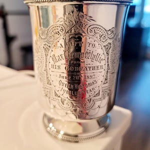 Puede incluir: Una copa de plata con una inscripci&oacute;n que dice "A Gift to Max Henry Wylie from His Godfather on June 20th 1887 Queen Victoria's Jubilee Year".