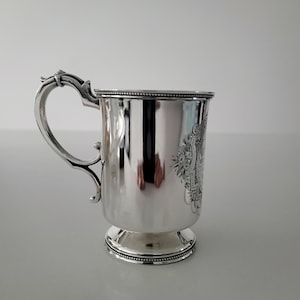 Puede incluir: Una taza de plata con un asa decorativa y un dise&ntilde;o grabado detallado. La taza tiene una base redonda y un acabado liso y pulido.