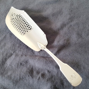 May include: A silver fish server with a decorative, openwork design on the blade. The handle has a simple, elegant shape with a small emblem. The server is made of a shiny, reflective metal.