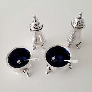 Puede incluir: Un juego de cuatro saleros y pimenteros de plata y saleros. Los saleros tienen un interior azul oscuro e incluyen cucharas pequeñas. Los pimenteros tienen una parte superior perforada. Un clásico para la mesa.