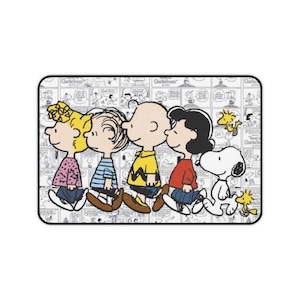 Peut inclure: Tapis de souris rectangulaire avec une image de dessin animé des personnages de Peanuts : Sally, Linus, Charlie Brown, Lucy et Snoopy. Le fond est un motif de bande dessinée en noir et blanc. Les personnages sont en couleur.