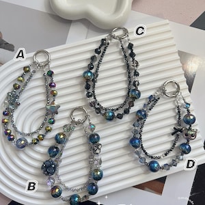 May include: Four handmade beaded bracelets with silver-tone clasps. Each bracelet features a unique design with iridescent beads, crystals, and decorative charms. The bracelets are displayed on a white, textured surface.