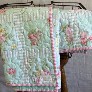 May include: A handmade quilt with a floral and striped pattern in shades of light blue, pink, and white. The quilt has a pink striped border and a label that reads "handmade by Pattie Mamas".