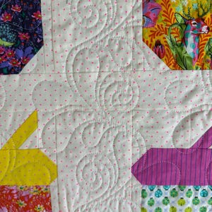 Puede incluir: Primer plano de un edred&oacute;n de patchwork colorido con un fondo blanco salpicado de lunares rosas. El edred&oacute;n presenta varios patrones de tela, incluyendo dise&ntilde;os florales, a rayas y geom&eacute;tricos. El patr&oacute;n de acolchado incluye l&iacute;neas onduladas y curvas.