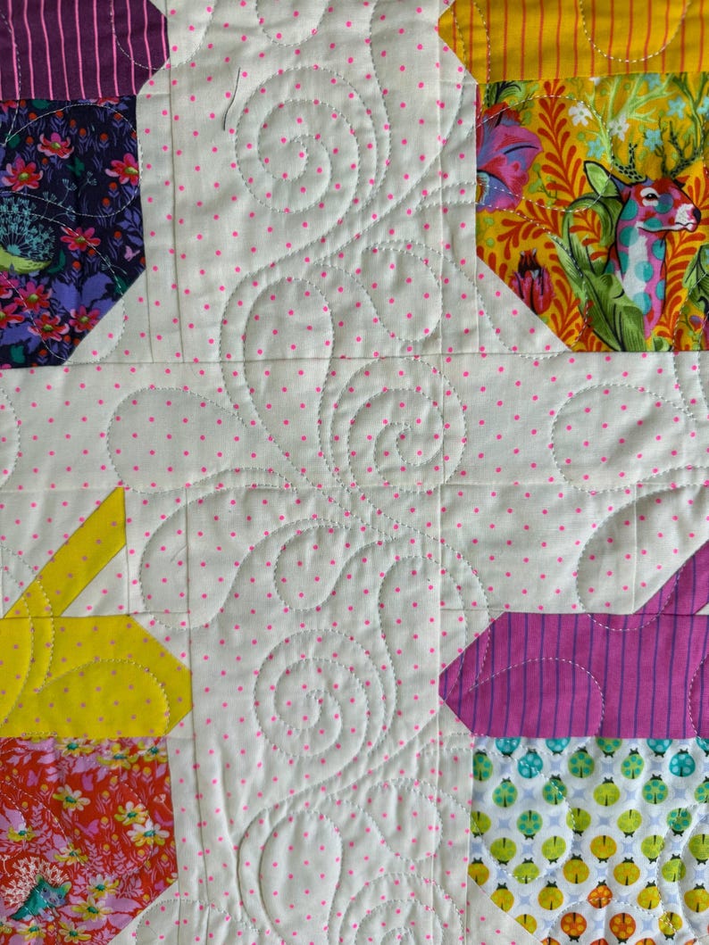 Puede incluir: Primer plano de un edred&oacute;n de patchwork colorido con un fondo blanco salpicado de lunares rosas. El edred&oacute;n presenta varios patrones de tela, incluyendo dise&ntilde;os florales, a rayas y geom&eacute;tricos. El patr&oacute;n de acolchado incluye l&iacute;neas onduladas y curvas.