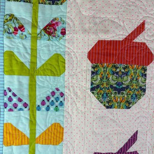 Puede incluir: Primer plano de un edred&oacute;n colorido con un patr&oacute;n floral y geom&eacute;trico. El edred&oacute;n presenta varios patrones de tela, incluyendo florales, a rayas y lunares. La paleta de colores incluye tonos de azul, verde, rojo, amarillo y morado. El edred&oacute;n est&aacute; acolchado a m&aacute;quina con una puntada decorativa.