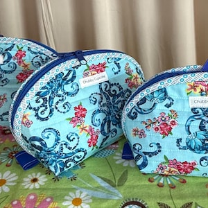 May include: Three quilted cosmetic bags with a light blue background, featuring a pattern of blue octopus designs and pink floral accents. Each bag has a zipper closure and a small label that reads "Chubby Cupcake".