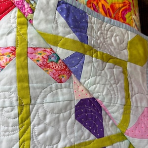 Puede incluir: Primer plano de un edred&oacute;n colorido con un dise&ntilde;o de patchwork. El edred&oacute;n presenta un fondo azul claro con formas geom&eacute;tricas en morado, rosa y amarillo. El edred&oacute;n tiene un estampado floral en la capa superior y est&aacute; cosido con un patr&oacute;n decorativo.