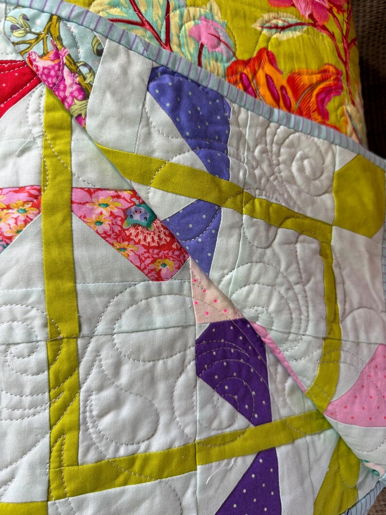 Puede incluir: Primer plano de un edred&oacute;n colorido con un dise&ntilde;o de patchwork. El edred&oacute;n presenta un fondo azul claro con formas geom&eacute;tricas en morado, rosa y amarillo. El edred&oacute;n tiene un estampado floral en la capa superior y est&aacute; cosido con un patr&oacute;n decorativo.
