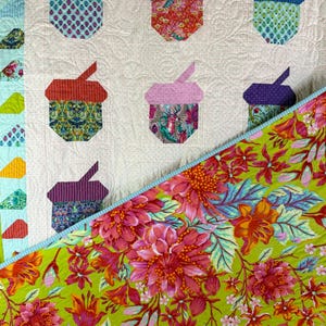Puede incluir: Un edred&oacute;n colorido con formas de bellotas aplicadas en varias telas estampadas. El edred&oacute;n tiene un fondo blanco con un borde floral y un reverso floral verde vibrante. Las bellotas son en tonos de azul, verde, rojo y morado.