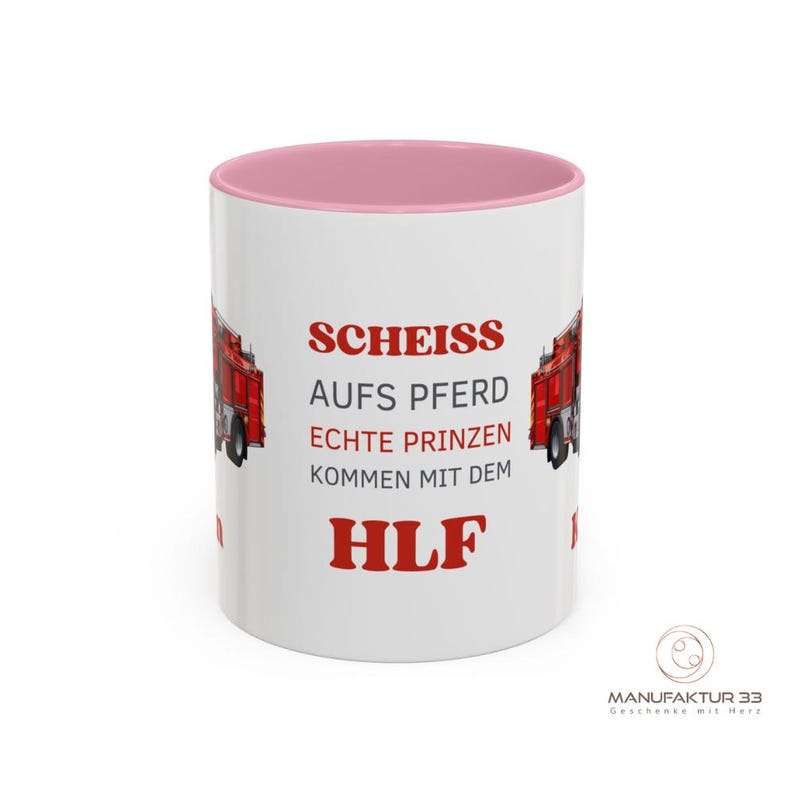 May include: White ceramic mug with a pink interior and the text "SCHEISS AUFS PFERD ECHTE PRINZEN KOMMEN MIT DEM HLF" in red. The mug features a red fire truck graphic on each side. The bottom right corner has a logo.
