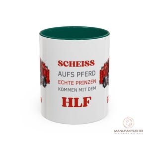 May include: White ceramic mug with a green interior and a red fire truck graphic. The mug features the text "SCHEISS AUFS PFERD ECHTE PRINZEN KOMMEN MIT DEM HLF" in red, with the brand logo "MANUFAKTUR 33" at the bottom.