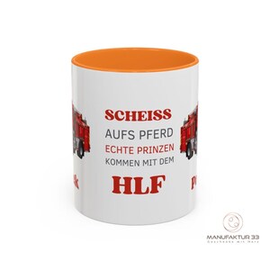 May include: White ceramic mug with an orange interior. The mug features red text and a red fire truck graphic. The text reads "SCHEISS AUFS PFERD ECHTE PRINZEN KOMMEN MIT DEM HLF".