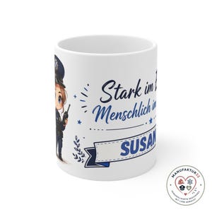 Könnte beinhalten: Ein weißer Keramikbecher mit einer Cartoon-Illustration einer Polizeikraft in Uniform, die ein Funkgerät hält. Der Text lautet Stark im Einsatz, Menschlich im Umgang, und der Name SUSANNE steht auf einem blauen Banner mit Sternen und Blättern.