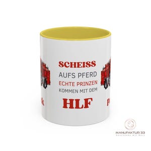 May include: White ceramic mug with a yellow interior and a red fire truck graphic. The mug features red text that reads "SCHEISS AUFS PFERD ECHTE PRINZEN KOMMEN MIT DEM HLF".