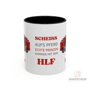 May include: White ceramic mug with a black interior and a red fire truck graphic. The mug features red text that reads "SCHEISS AUFS PFERD ECHTE PRINZEN KOMMEN MIT DEM HLF". The mug has a glossy finish.